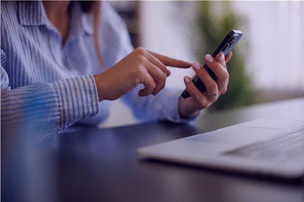 Woman in striped shirt holding a mobile phone with an open banking/financial app.